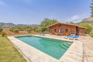A wooden cabin with a swimming pool, blue lounge chairs, and a stone patio.