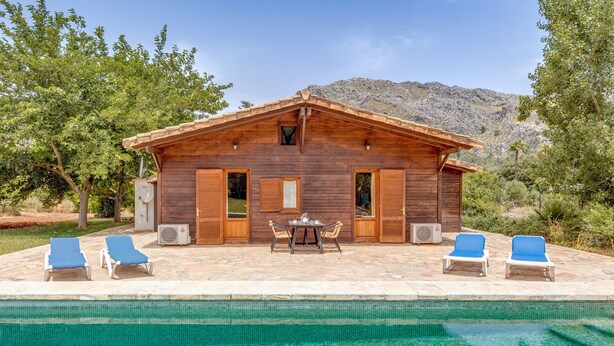 Een houten chalet met een zwembad, lounge stoelen en een tafel.