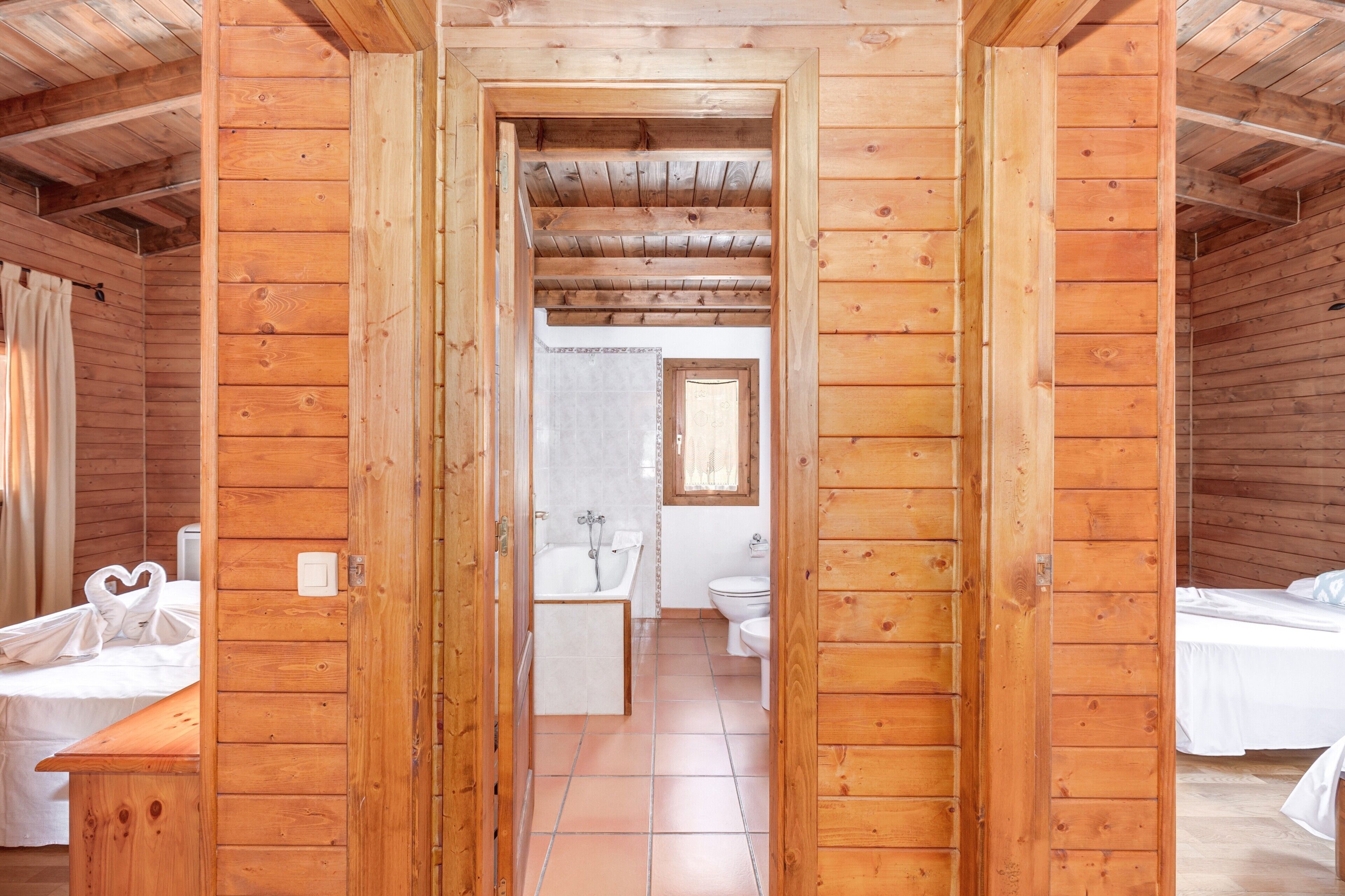 A wooden cabin interior with a bathroom, a bed, and a bench.