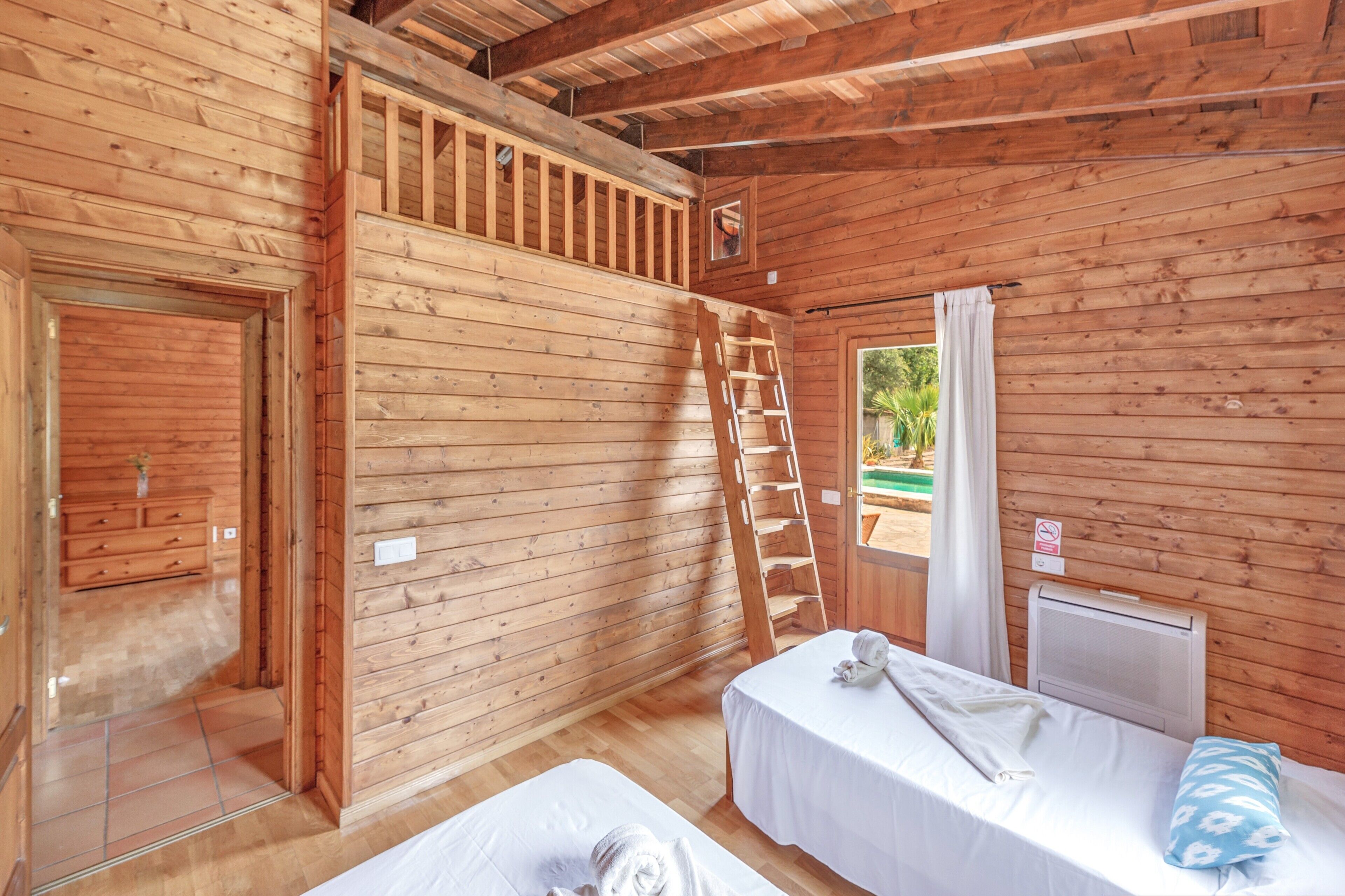 Une cabane en bois avec deux lits, une échelle et une fenêtre avec des rideaux.