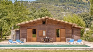 Een houten chalet met zwembad, twee ligstoelen en een tafel.