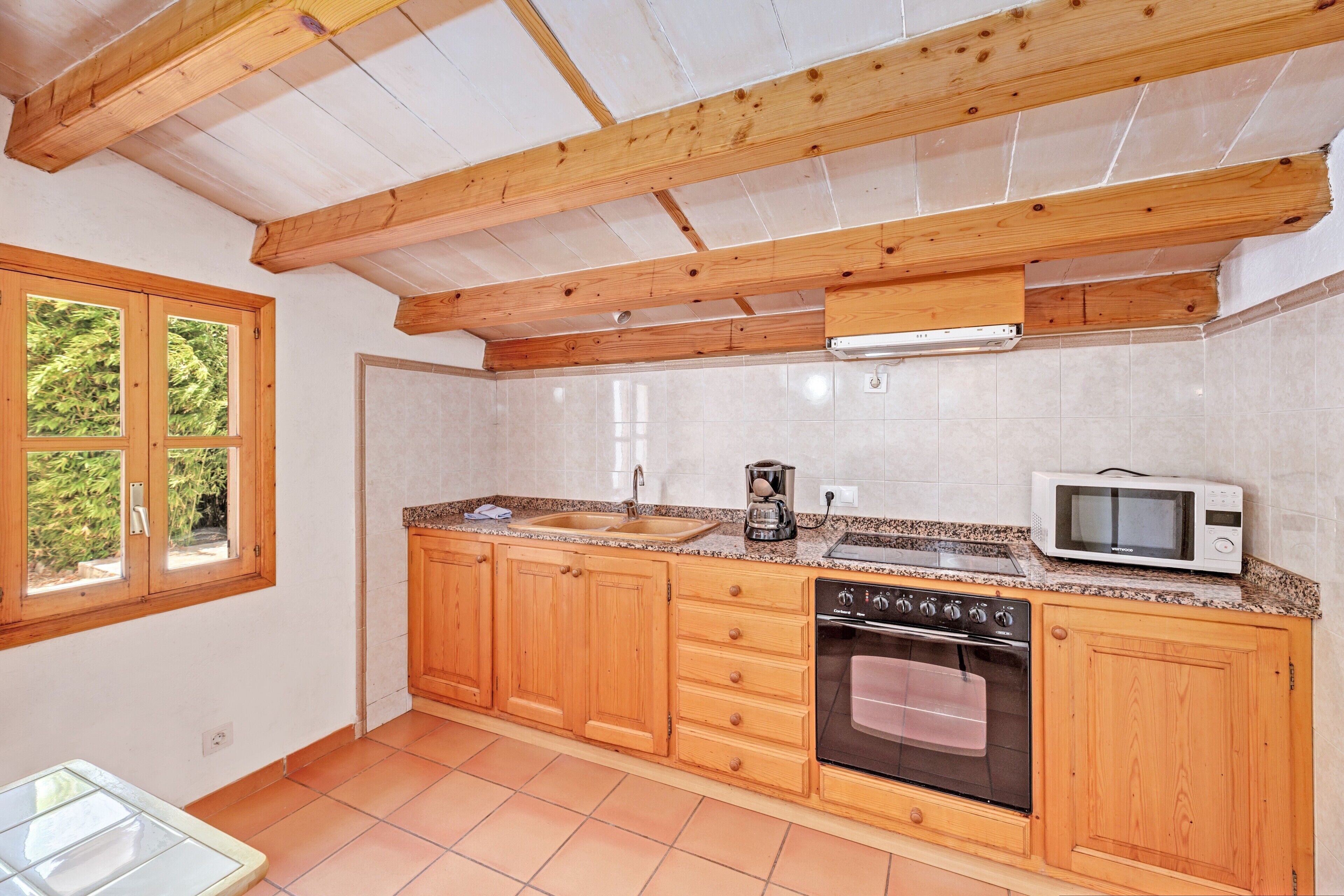Una cocina con armarios de madera, microondas, horno y ventana con vistas al verde.