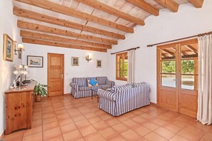 A room with wooden beams, a sofa set, a wooden cabinet, and a window with curtains.