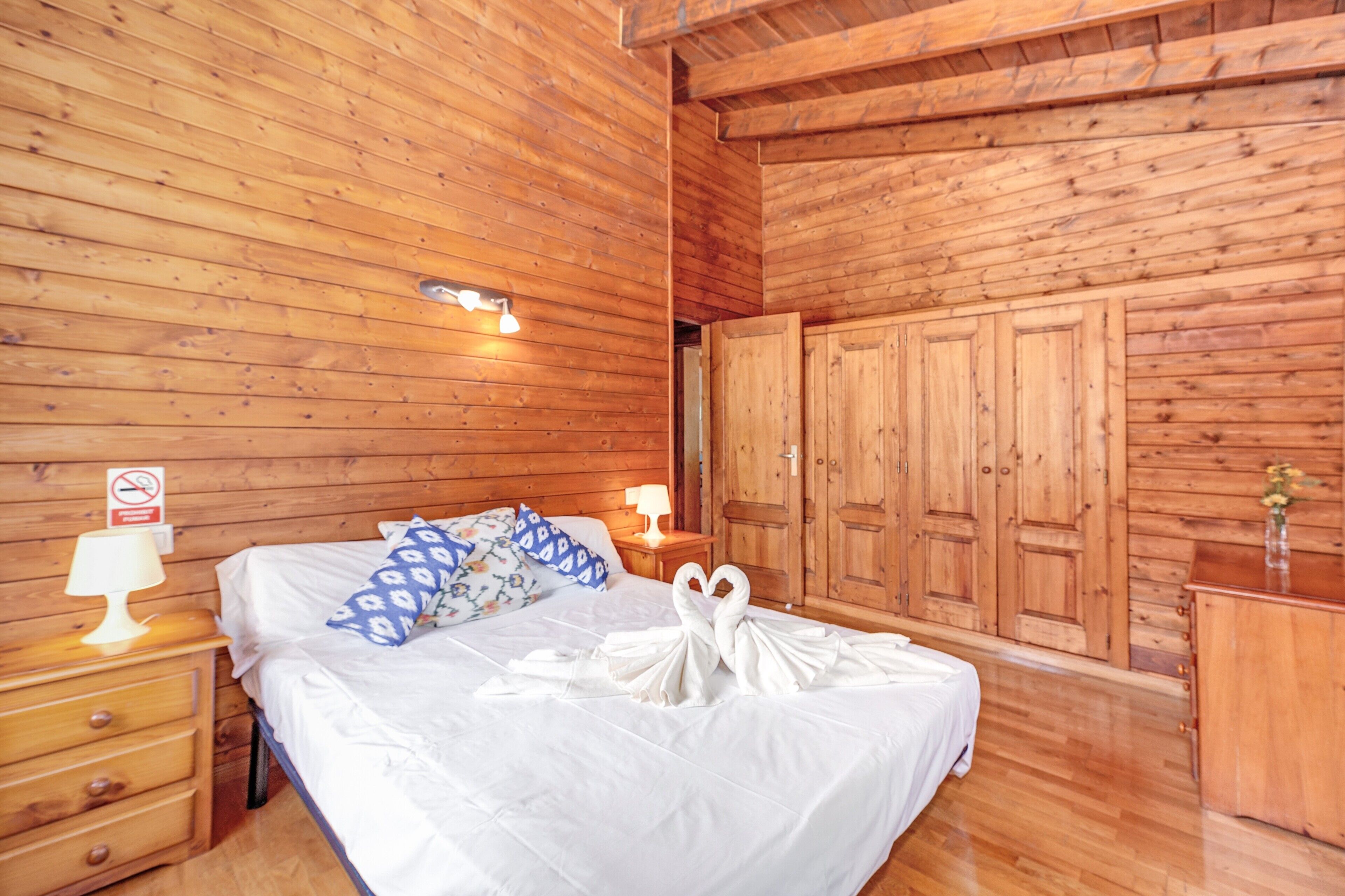 Una habitación con paneles de madera, con cama, mesitas de noche, cómoda y armario.