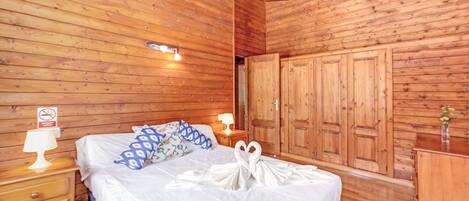 Una habitación con paneles de madera, con cama, mesitas de noche, cómoda y armario.