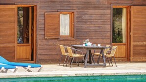 Een houten hut met een zwembad, een tafel met stoelen en een blauwe ligstoel.