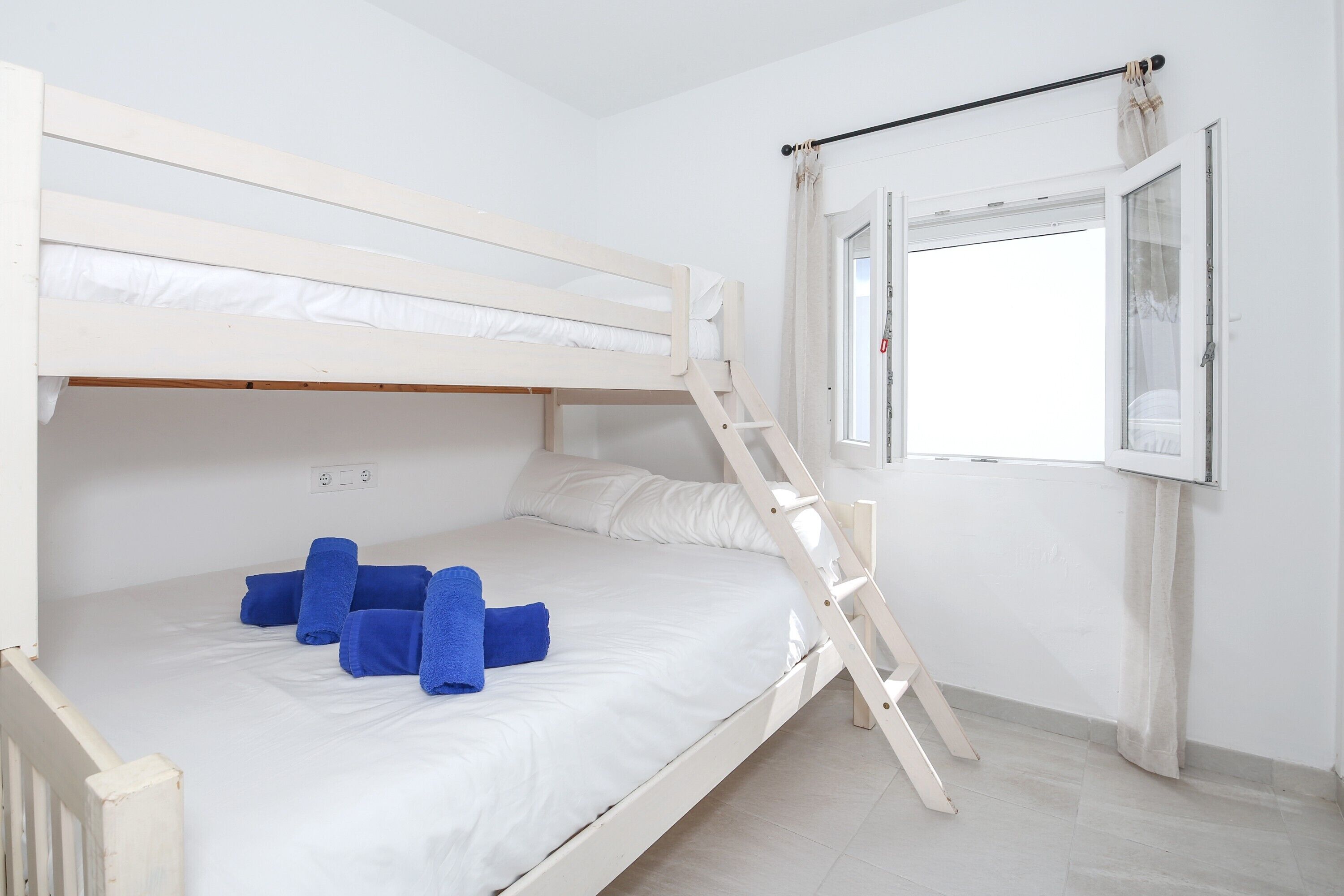 Een stapelbed met een ladder, een raam met gordijnen en een witte muur.