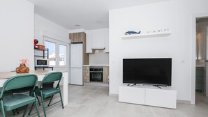 Eine moderne Küche mit integriertem Fernseher, einem Essbereich mit grünen Stühlen und einer weißen Arbeitsplatte.