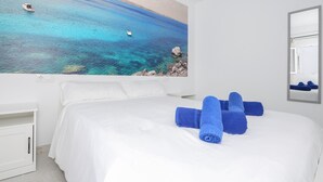 Ein Hotelzimmer mit einem großen Bett, weißer Bettwäsche und einem Gemälde einer Küstenlandschaft.