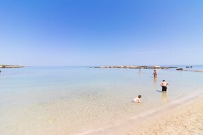 A beach with clear water, people swimming, and a sandy shore.