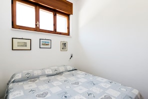 Una camera da letto con un letto, una finestra con persiane in legno e tre quadri appesi al muro.