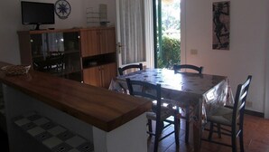 A kitchen with a dining table, chairs, a television, and a window with curtains. - Apartment "Golfo Stella" With Sea View and Near the Sea (CAPOLIVERI)
