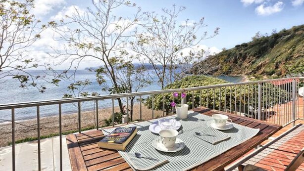 Une terrasse en bois avec une table dressée pour deux personnes, offrant une vue sur la plage et la mer.