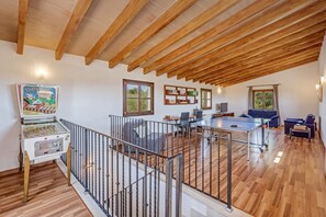 A spacious loft with exposed wooden beams, a ping pong table, a sofa, and a small kitchen area.