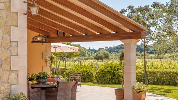 Eine Terrasse im Freien mit einer Pergola, Korbmöbeln und Topfpflanzen.