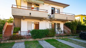 Un immeuble résidentiel de deux étages doté d’un balcon, d’un escalier et d’un petit jardin.