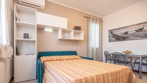 Une chambre à coucher comprenant un lit, un bureau, des chaises, une étagère et un tableau accroché au mur.
