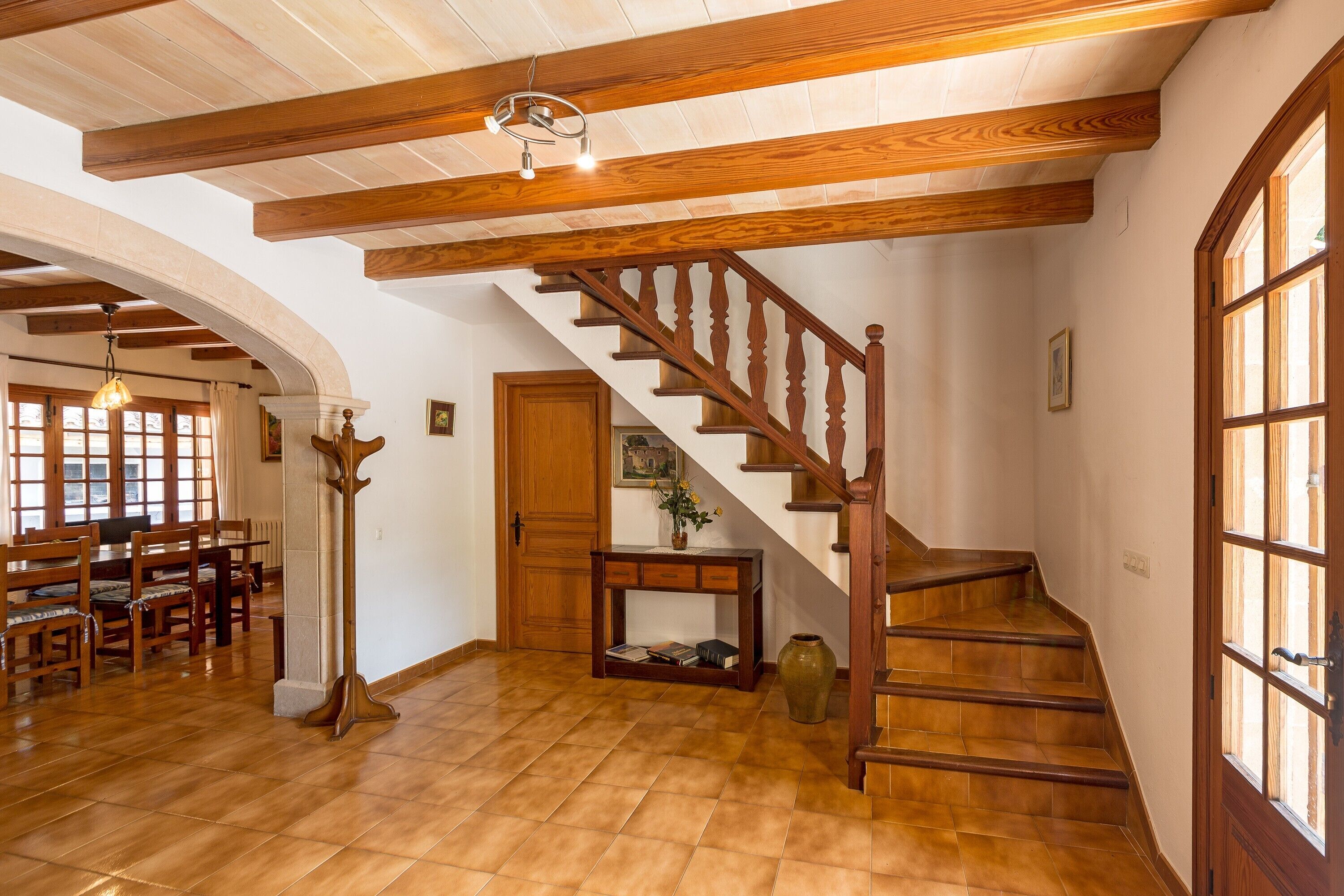 Un escalier en bois avec une console et un vase, un coin repas avec des chaises et une table, et une grande fenêtre.