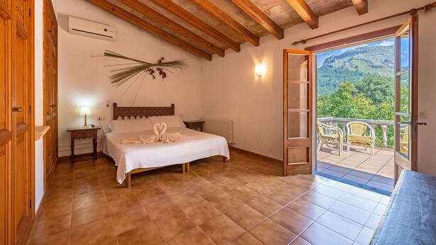 A bedroom with a bed, a nightstand, a lamp, a radiator, and a view of a balcony with chairs. - Villa "La Plana" with Stunning Mountain Panorama and Pool (Pollensa)