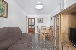 Una habitación con un sofá marrón, una mesa de comedor de madera con sillas, un televisor y un ventilador de techo.