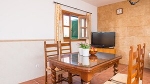 A dining area with a glass-top table, wooden chairs, a television, and a window with curtains.