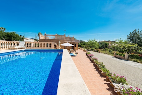 Een zwembad met helderblauw water, een terras met stoelen en een tafel, en een groot gebouw met een balkon op de achtergrond.. Family-Friendly Villa "Ses Llegitimes" with Pool