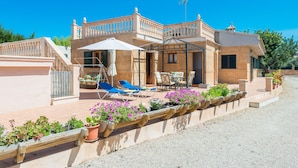 A two-story building with a balcony, outdoor seating, and a garden with potted plants.