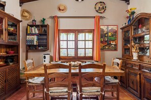 Een eetruimte met een houten tafel en stoelen, omringd door houten kasten en planken met boeken en decoratieve objecten.