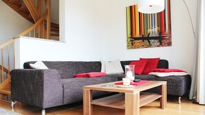 A modern living room with a grey sofa, a wooden coffee table, and a colorful abstract painting on the wall. - Beach house, 200 sqm. Wf., Directly at the Plauer See, Müritz, 30m to the beach (Fünfseen Lenz Süd)
