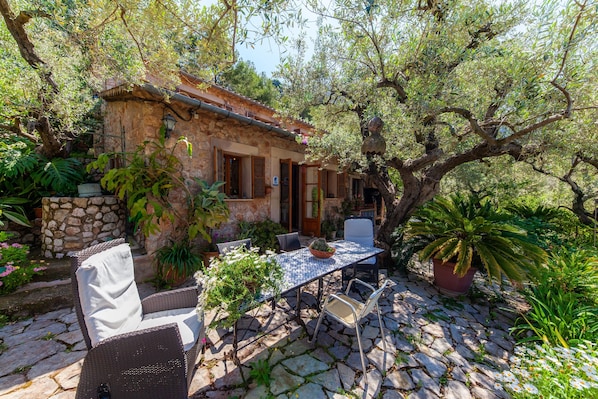 A stone building with a tiled patio, outdoor seating, and lush greenery.