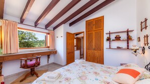 Un dormitorio con cama, escritorio, silla, armario y ventana con cortinas.