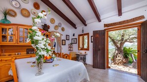 Un comedor con una mesa dispuesta para dos, un armario de madera con puertas de cristal y vistas a un árbol a través de un ventanal.