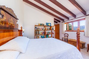 A bedroom with a wooden bed, a bookshelf, a window with curtains, and a view of the outdoors.