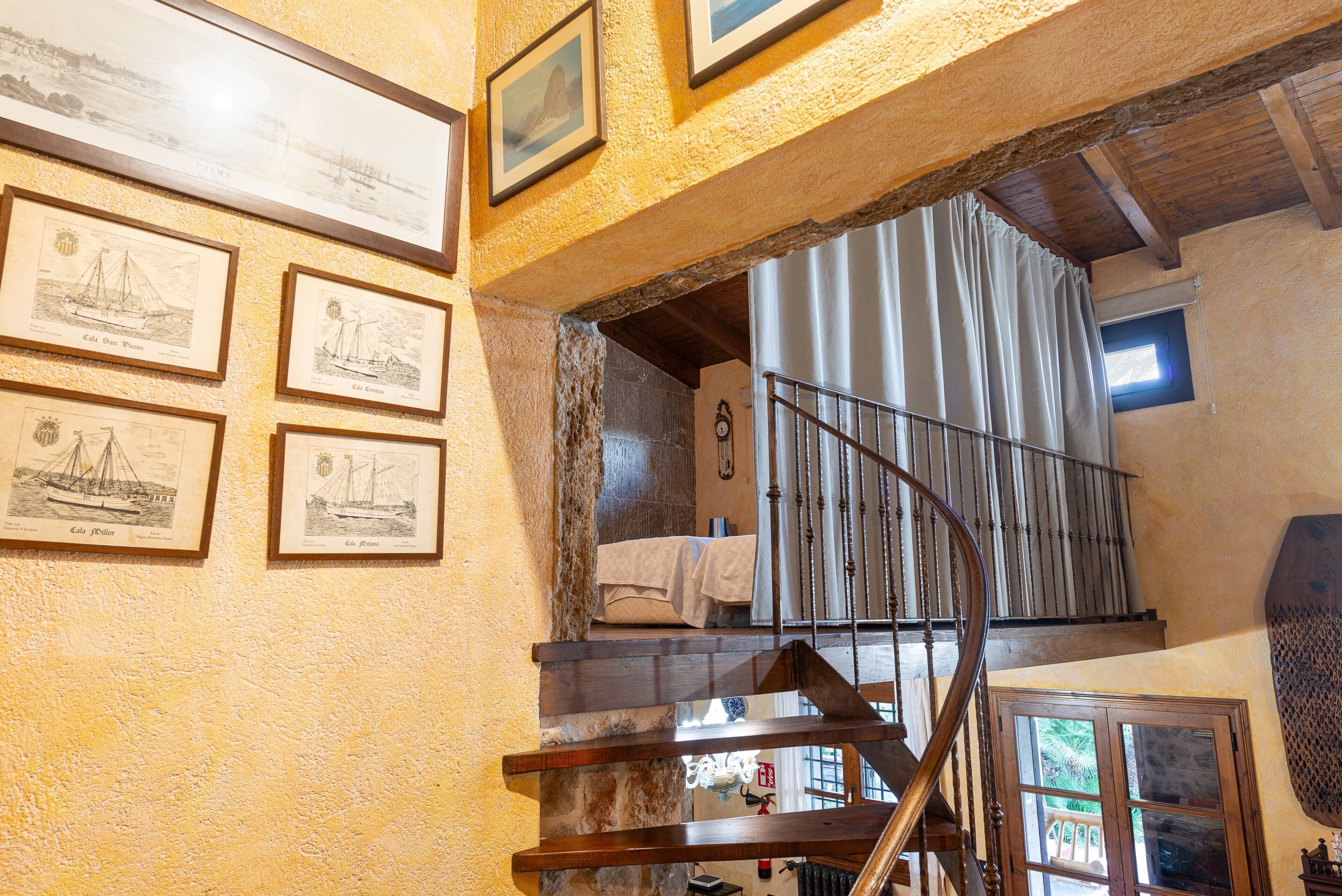 A room with a wooden staircase, a bed with a white blanket, and framed maritime illustrations on the wall.