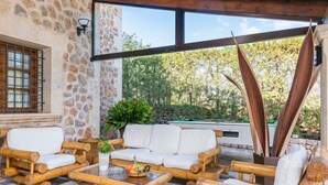 An outdoor seating area with bamboo furniture, a stone wall, and a view of trees. - Villa with mountain view and pool - Es Puchet (Alcudia)