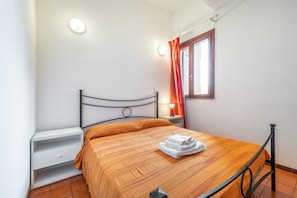 Un lit bien fait, recouvert d’une couvre-lit à rayures, une table de chevet avec une lampe et une fenêtre avec des rideaux.