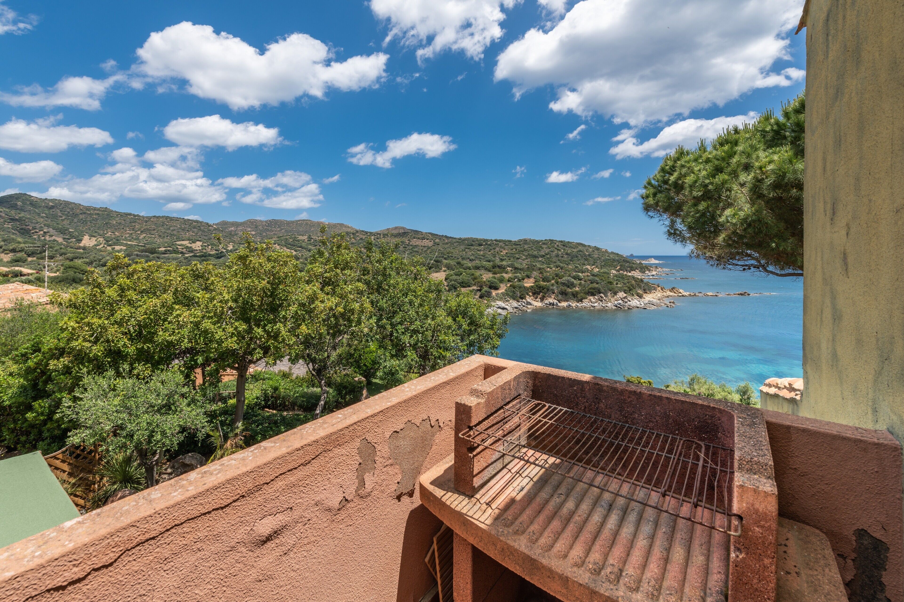 Ein Balkon mit Grill, der auf eine Küstenlandschaft mit Bäumen und Hügeln blickt.