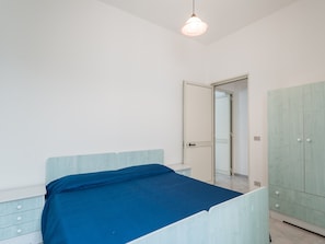 A bedroom with a bed, a wardrobe, a bedside table, and a door leading to another room.