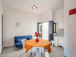 A dining area with a table, chairs, a vase with flowers, a blue sofa, and a kitchen in the background.