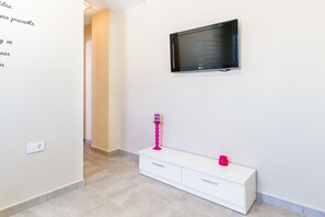 A hallway with a white console table, a flat-screen TV mounted on the wall, and a pink candle holder on the table.