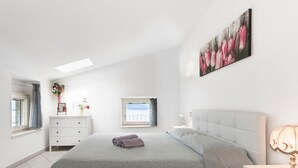 Ein Schlafzimmer mit Bett, Nachttisch, Schminktisch, Fenster und einem Gemälde an der Wand.
