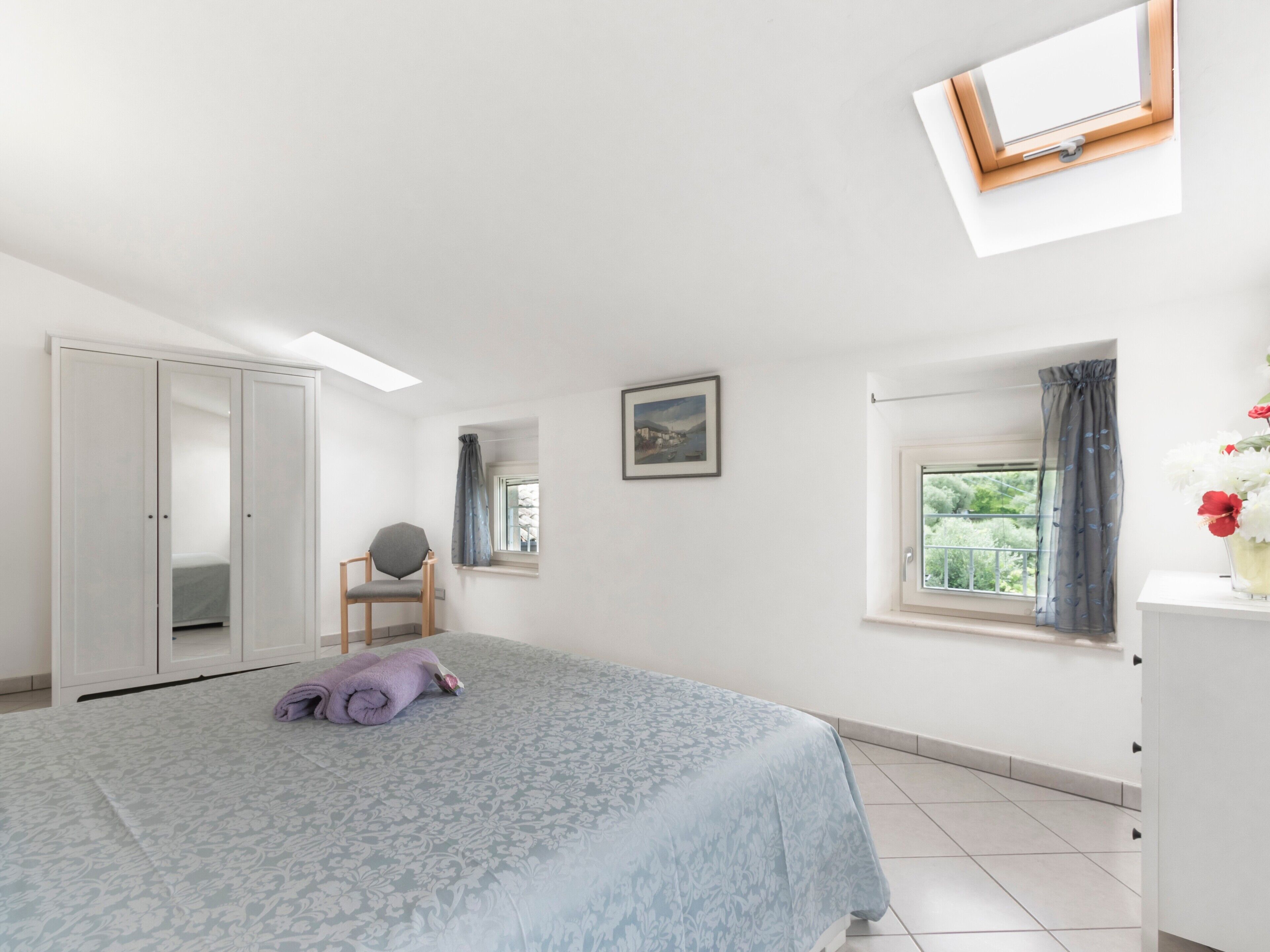 Ein Schlafzimmer mit Bett, Sessel, Fenster mit Blick, einem Gemälde und einem Kleiderschrank.