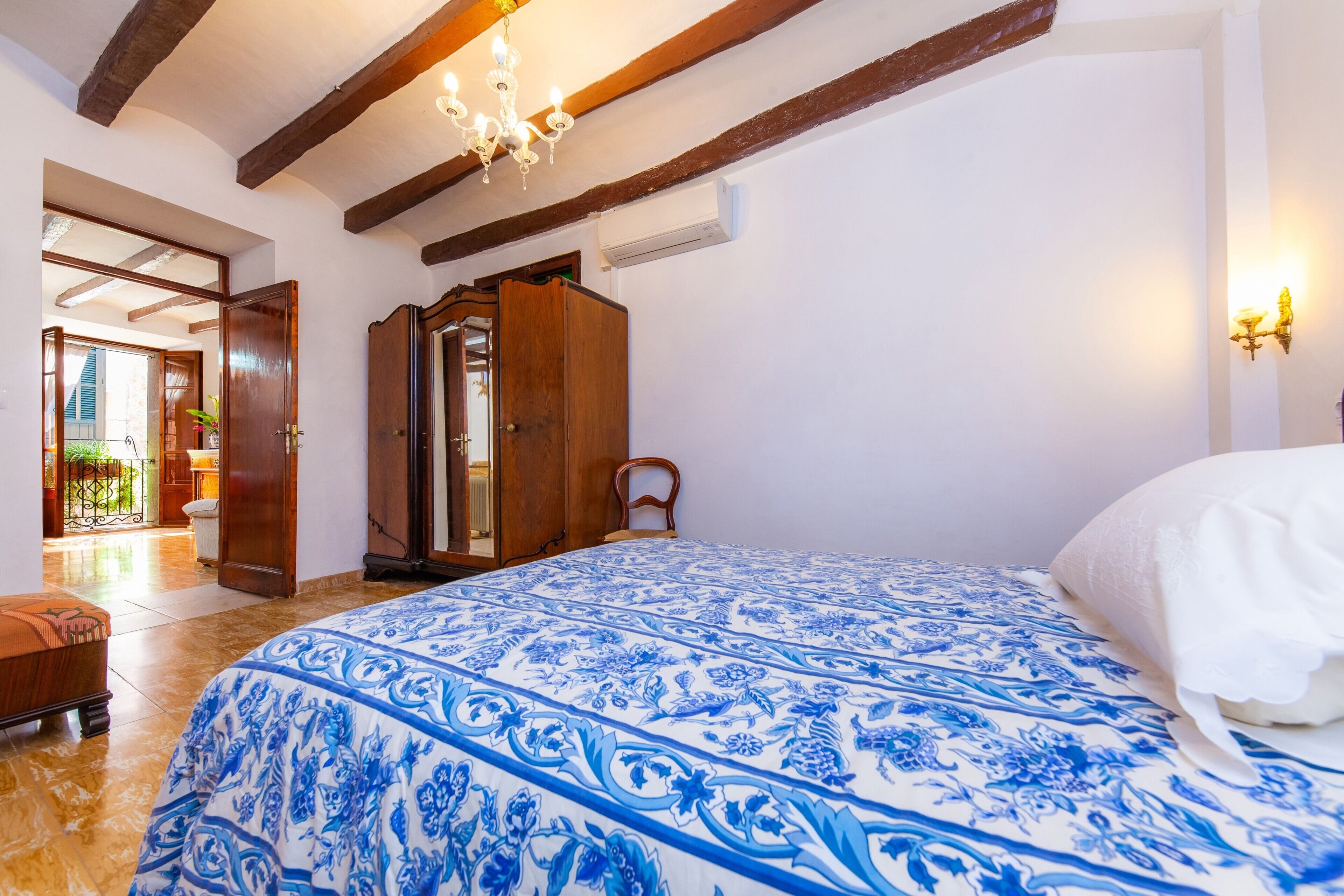 A bedroom with a large bed, wooden beams, a chandelier, and a view of the outside.