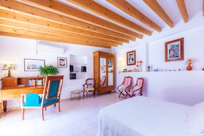 Een kamer met een houten plafond, een bed, een bureau met stoel, een kledingkast en een spiegel.