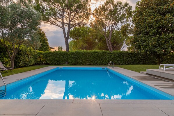 A rectangular swimming pool with a clear blue water surface, surrounded by a paved deck and a well-maintained hedge.