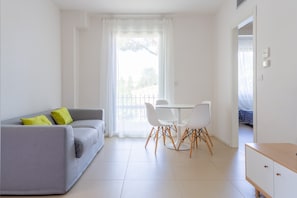 Ein modernes Wohnzimmer mit grauem Sofa, weißem Esstisch und Stühlen.