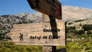 Un poste de madera con indicaciones direccionales, símbolos de senderismo y texto que muestra las distancias a varios destinos.