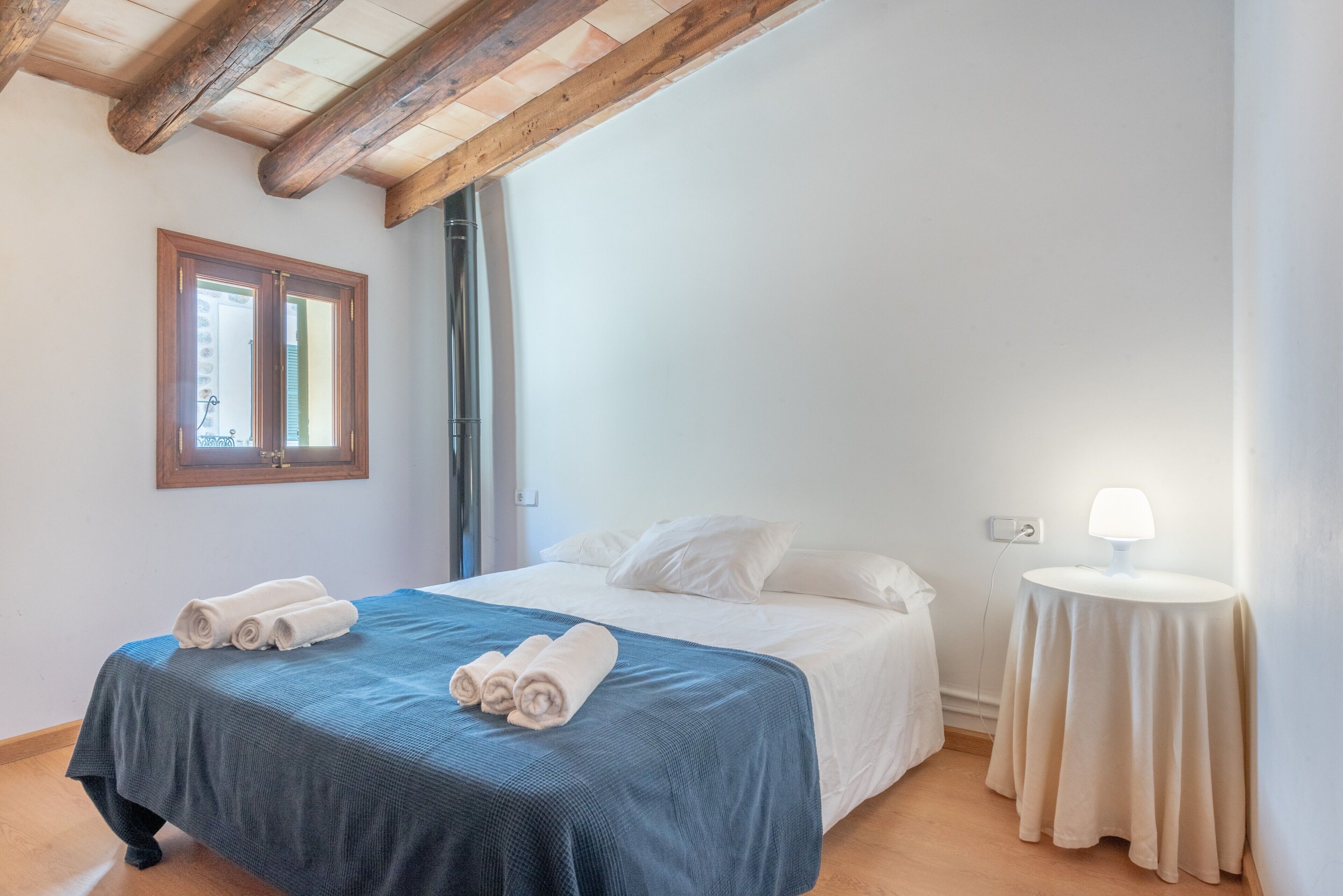 Une chambre à coucher avec un lit, une fenêtre, une table de chevet avec une lampe et des serviettes pliées sur le lit.