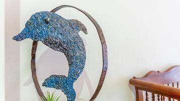 Une sculpture en métal représentant un dauphin, posée sur un socle circulaire, une chaise en bois et une petite plante au premier plan.