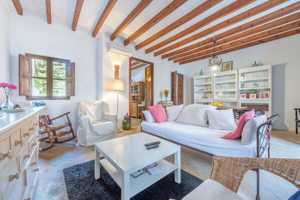 A spacious living room with a white sofa, a wooden rocking chair, a white coffee table, and a bookshelf.
